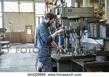 Stock Photo - Caucasian man using drilling machine in metal shop. Fotosearch