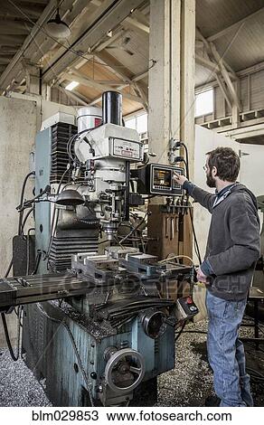 Stock Image - Caucasian man using machinery in metal shop. Fotosearch