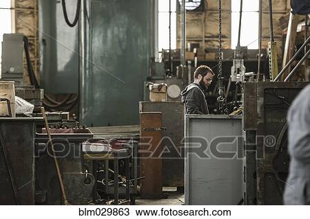 Stock Image - Caucasian man using machinery in workshop. Fotosearch