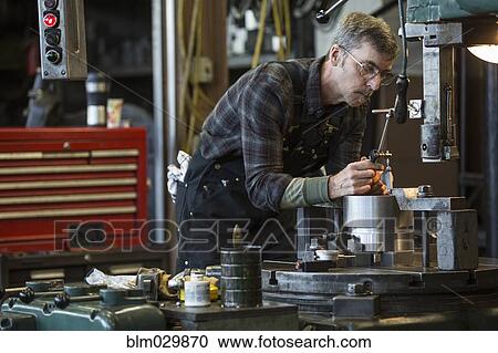 Stock Image - Caucasian man using machinery in workshop. Fotosearch