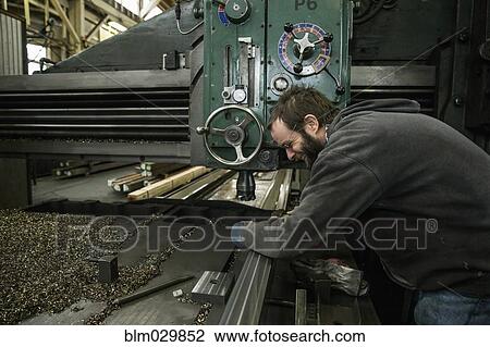 Stock Image - Caucasian man working at machinery in metal shop. Fotosearch