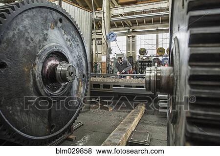 Caucasian man working behind metal cogs in metal shop View Large Photo Image Stock Photo - Caucasian man working behind metal cogs in metal shop. Fotosearch