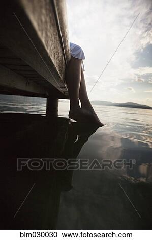 Stock Image - Caucasian woman dipping feet in still lake. Fotosearch