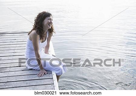 Stock Image - Caucasian woman on wooden dock on still lake. Fotosearch