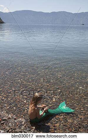 Stock Photo - Caucasian woman wearing mermaid costume in still lake. Fotosearch