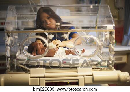 Stock Image - Nurse tending to newborn in incubator. Fotosearch