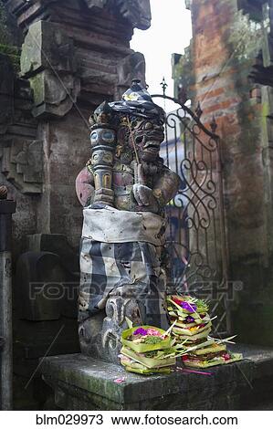 Stock Image - Offerings at base of Hindu statue, Ubud, Bali, Indonesia. Fotosearch