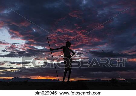 Stock Photograph - Silhouette of boy with walking stick under sunset sky, Nyangaton, Ethiopia. Fotosearch