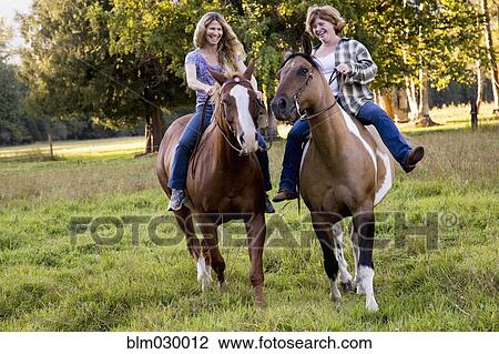 Stock Image - Women riding horses in rural landscape. Fotosearch