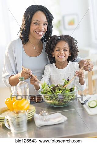 Stock Image - African American mother and daughter tossing salad. Fotosearch
