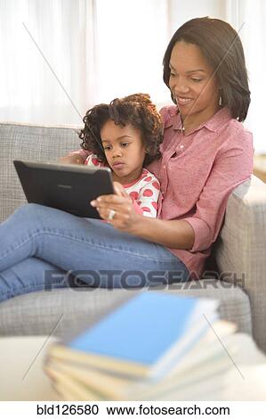 Black mother and daughter using digital tablet on sofa View Large Photo Image Stock Image - Black mother and daughter using digital tablet on sofa. Fotosearch