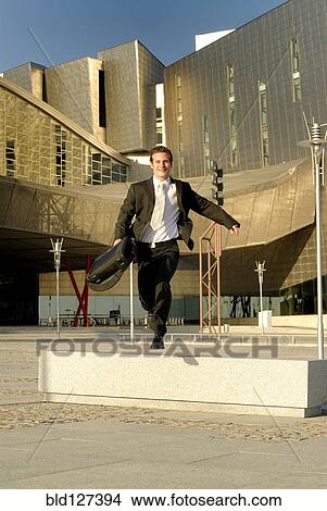 Businessman jumping bench in front of modern office building View Large Photo Image Picture - Businessman jumping bench in front of modern office building. Fotosearch
