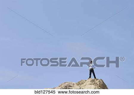 Businessman standing on top of rock looking into distance View Large Photo Image Stock Photography - Businessman standing on top of rock looking into distance. Fotosearch