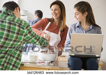 Stock Image - Caucasian family baking and using laptop in kitchen. Fotosearch