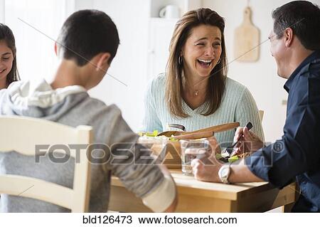 Stock Image - Caucasian family laughing and eating at table. Fotosearch