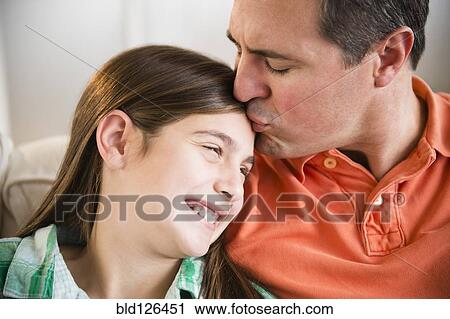 Stock Image - Caucasian father kissing daughter's forehead. Fotosearch