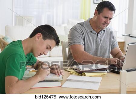 Stock Photography - Caucasian father using laptop near studying son. Fotosearch