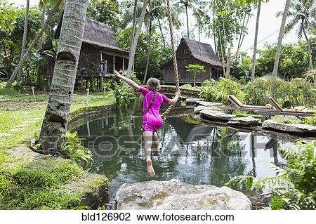 Stock Image - Caucasian girl swinging on rope in garden, Ubud, Bali, Indonesia. Fotosearch