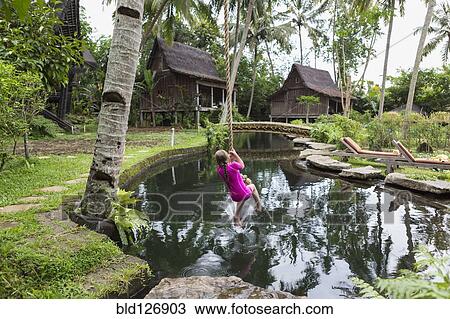 Stock Image - Caucasian girl swinging on rope in garden, Ubud, Bali, Indonesia. Fotosearch