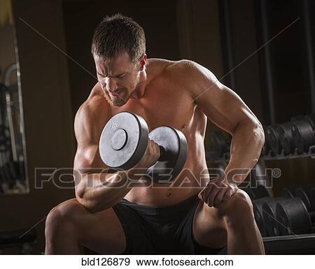 Stock Photo - Caucasian man doing biceps curls with dumbbell in gym. Fotosearch