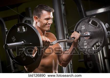 Stock Image - Caucasian man lifting barbell in gym. Fotosearch