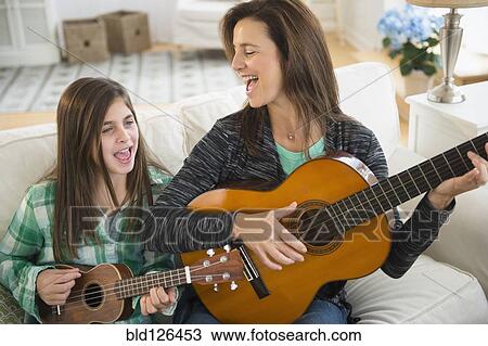 Stock Image - Caucasian mother and daughter singing with guitar and ukulele. Fotosearch