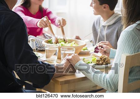 Stock Image - Caucasian parents holding hands at table. Fotosearch
