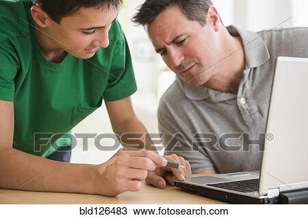 Stock Image - Caucasian son showing father how to use USB stick in laptop. Fotosearch