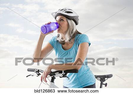 Stock Image - Caucasian woman drinking from water bottle on bicycle. Fotosearch