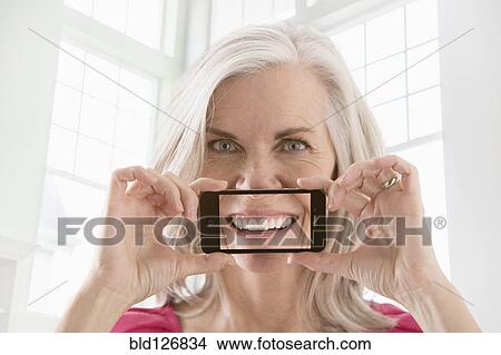 Caucasian woman holding cell phone with image of smile View Large Photo Image Picture - Caucasian woman holding cell phone with image of smile. Fotosearch