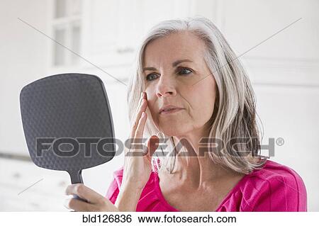 Stock Photograph - Caucasian woman looking at skin in mirror. Fotosearch