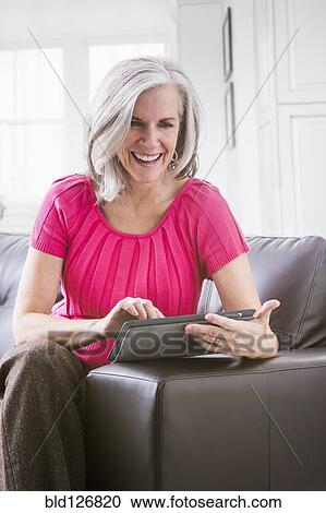 Stock Image - Caucasian woman using digital tablet on sofa. Fotosearch