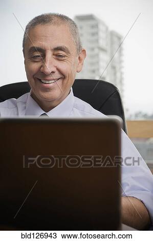 Stock Image - Close up of smiling Hispanic businessman using laptop. Fotosearch