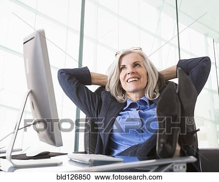 Stock Image - Confident Caucasian businesswoman with feet up on desk. Fotosearch