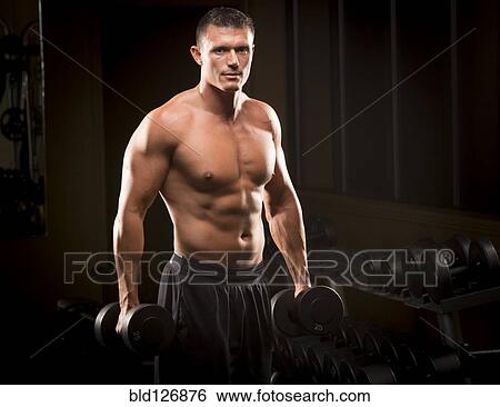 Stock Photograph - Confident Caucasian man holding dumbbells in gym. Fotosearch