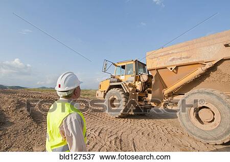 Stock Photo - construction worker looking at earth moving truck. Fotosearch