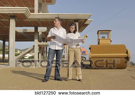 Stock Image - Couple looking at blueprints at construction site. Fotosearch