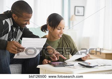 Stock Image - Couple paying bills in living room. Fotosearch