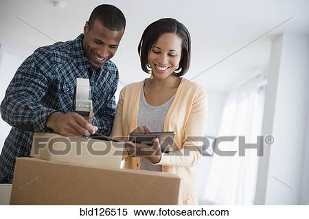 Couple with digital tablet taping up moving boxes View Large Photo Image Stock Photography - Couple with digital tablet taping up moving boxes. Fotosearch