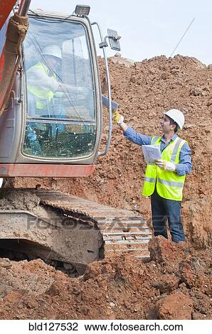 Stock Image - engineer handing plans to excavator driver. Fotosearch