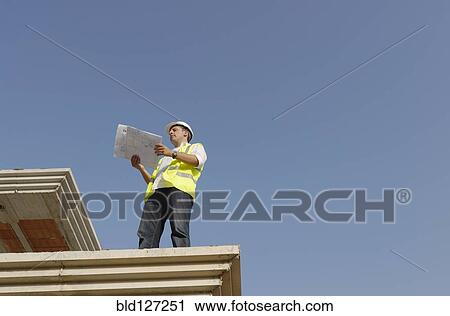 Engineer looking at plan on construction site low angle view View Large Photo Image Stock Image - Engineer looking at plan on construction site low angle view. Fotosearch