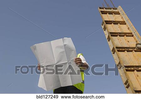 Engineer looking at plan on construction site low angle view View Large Photo Image Stock Photo - Engineer looking at plan on construction site low angle view. Fotosearch