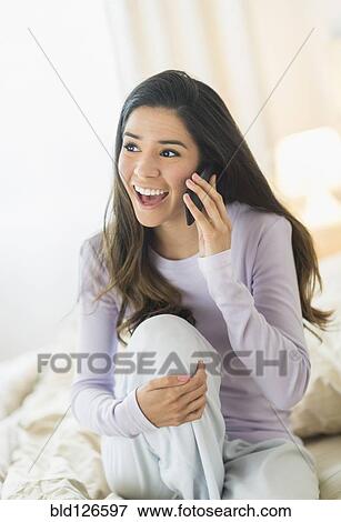 Enthusiastic Hispanic woman talking on cell phone in bed View Large Photo Image Stock Photo - Enthusiastic Hispanic woman talking on cell phone in bed. Fotosearch