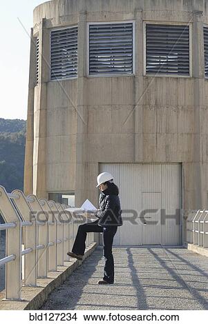 Female engineer looking at technical drawing outside hydro electric power station side view View Large Photo Image Picture - Female engineer looking at technical drawing outside hydro electric power station side view. Fotosearch