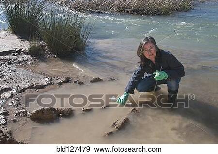 Stock Photo - female scientist taking water sample in stream. Fotosearch