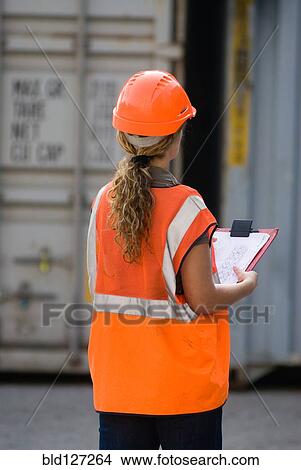 Female worker with clipboard checking containers in container terminal rear view View Large Photo Image Picture - Female worker with clipboard checking containers in container terminal rear view. Fotosearch