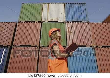 Stock Image - Female worker with clipboard in cargo container terminal low angle. Fotosearch