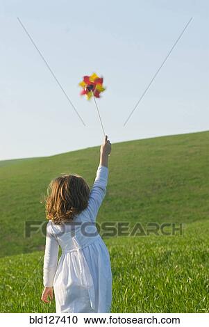 Stock Image - Girl holding up pinwheel in field. Fotosearch