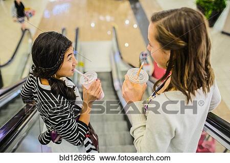 Girls drinking smoothies on escalator at shopping mall View Large Photo Image Stock Photography - Girls drinking smoothies on escalator at shopping mall. Fotosearch