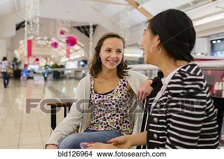 Picture - Girls talking on bench at shopping mall. Fotosearch